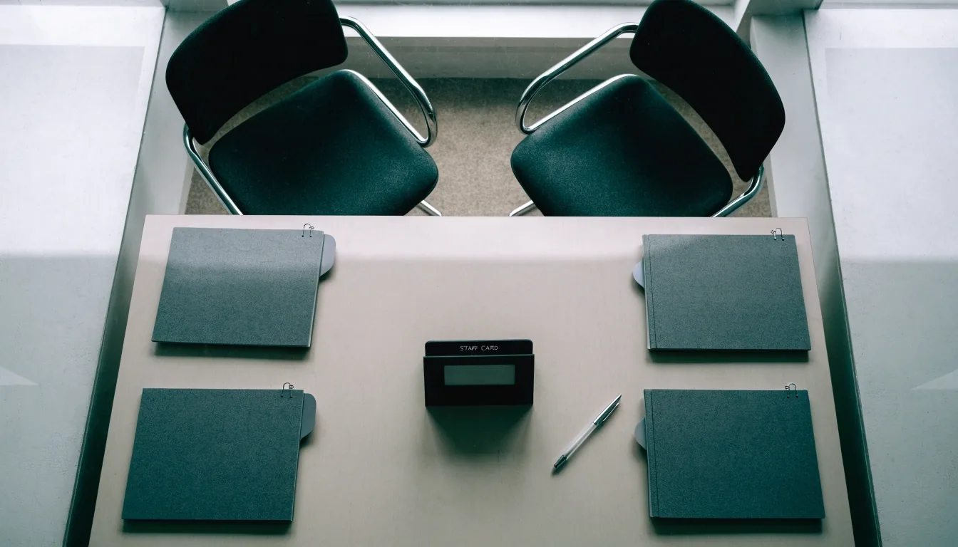 A documentation desk seen from above with closed binders and two chairs pulled up to the table